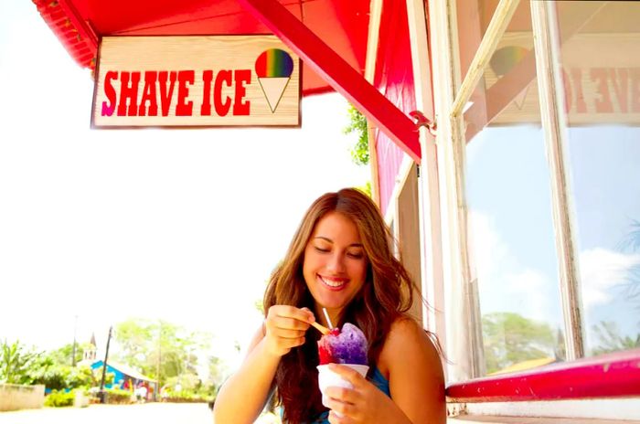 A woman enjoys shave ice outside a store in Hawaii, smiling with delight.