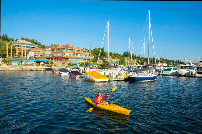 A woman paddling in a bright yellow kayak at Kirkland Marina, Seattle, with the city skyline in the background.