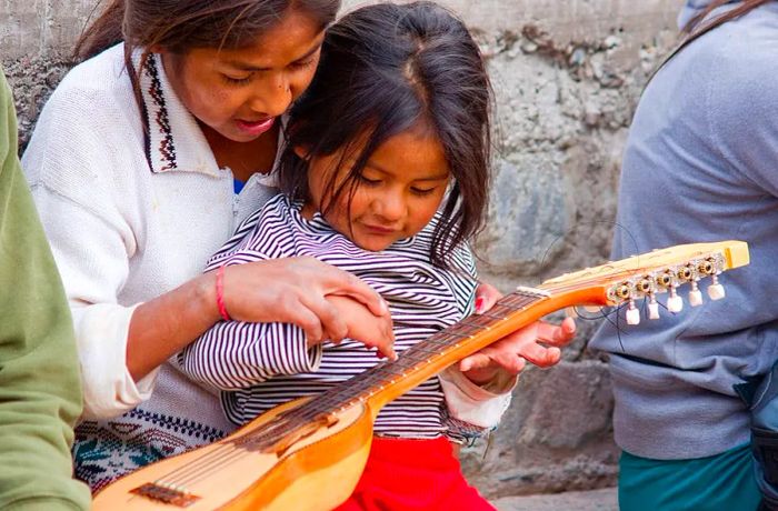 Young Quechua girls are playing with a charango, a traditional Andean lute, in Iruya, a remote village located in the Quebrada de Humahuaca in Northern Argentina.