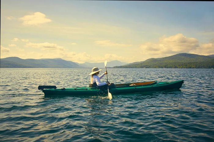 A woman paddles effortlessly across Lake George in a large kayak.