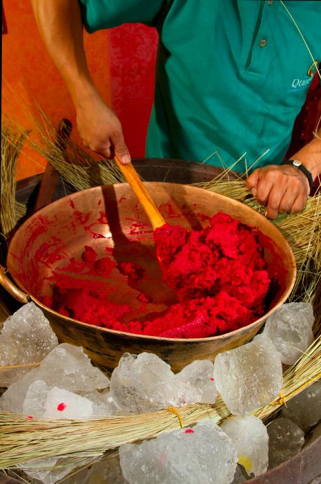 A person stirs dark pink ice cream in a bronze pot filled with ice in Ecuador