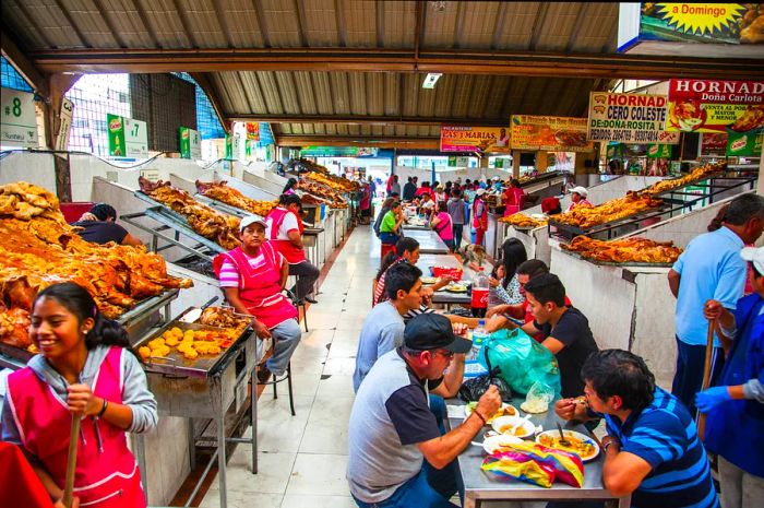 People enjoy pork dishes at long tables in a local Ecuadorian market