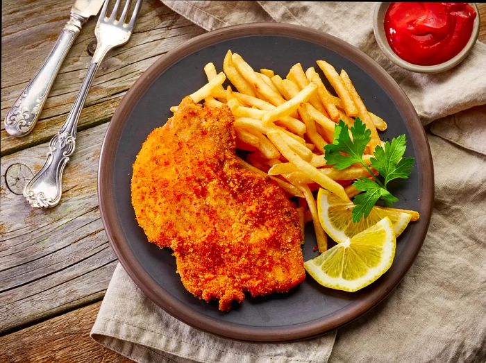 A rustic wooden table set with a plate of schnitzel, golden French fries, and fresh lemon slices