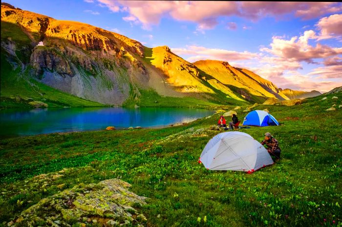 A group of hikers sets up camp with the stunning Ice Lake as their backdrop, surrounded by clouds in Colorado, USA