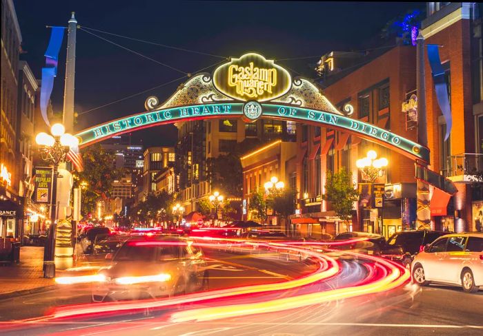 A nighttime photograph capturing a bustling street scene. A large banner hangs overhead,