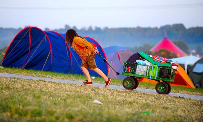 A festival-goer pulls a fully loaded trolley filled with camping gear up a hill at the campsite.