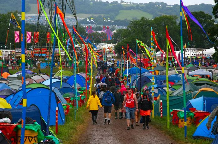 Festival-goers trudge along a muddy path between tents at the campsite.