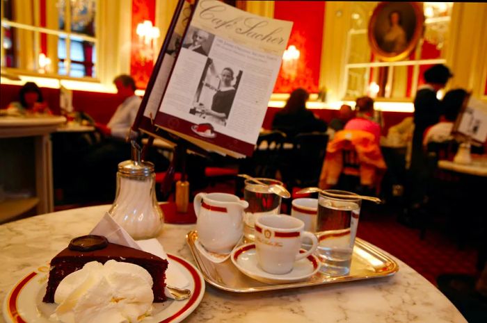 The elegant interior of Café Sacher in Vienna; a table is set with coffee cups and a milk jug, alongside a slice of the famous Sachertorte.