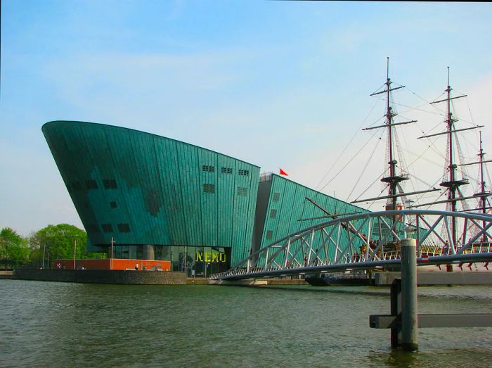 A large green building resembling a copper hull sits at the water's edge