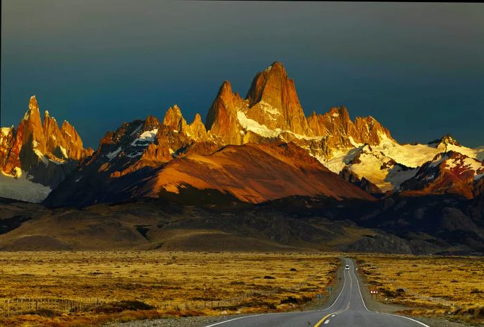 A deserted road leading towards sharply pointed mountain peaks