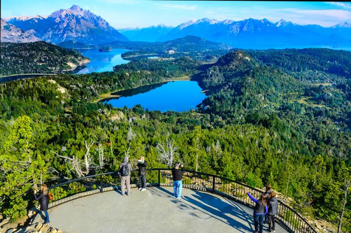 Viewers admiring lakes, forests, and mountains from a scenic overlook