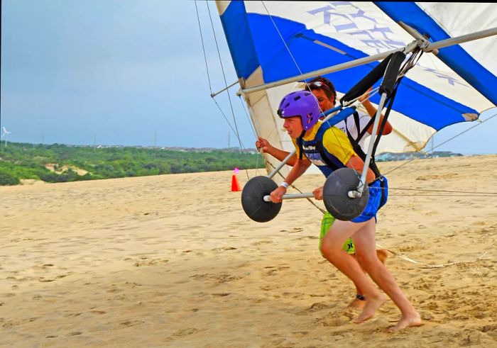 A teenager receives instructions for hang gliding from a kite on sandy dunes