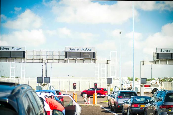 Numerous cars are queued, waiting to board the Eurotunnel trains, while overhead signs provide directions in both French and English.