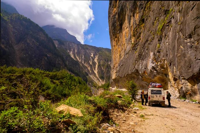 Travelers pausing at their off-road vehicle while navigating a mountain pass in Nepal.