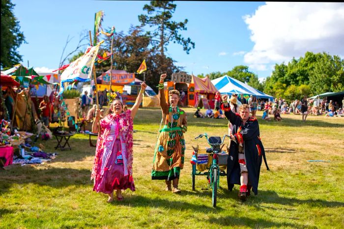 Festival attendees revel in a vibrant field adorned with colorful tents and flags during the Green Gathering festival in Wales.