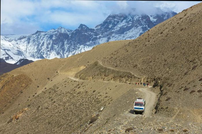 An aerial view of a bus with the majestic Himalayas in the background along the dusty road connecting Jomsom and Muktinath, Nepal.