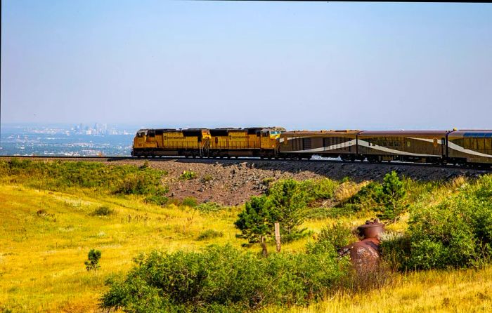 A train curves around a bend, with a city skyline visible in the distance