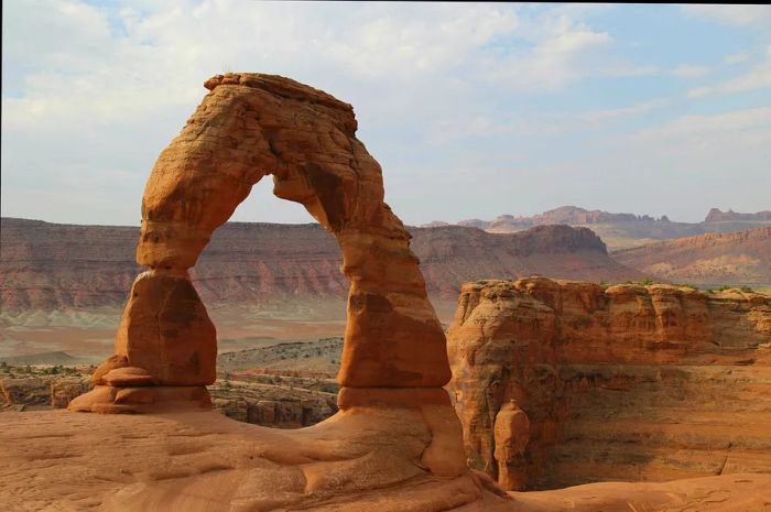 A sandstone arch framed by red rock cliffs under a bright blue sky