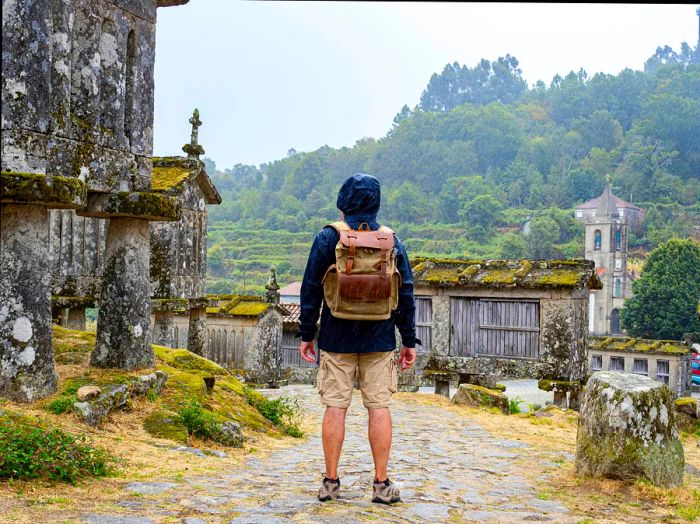 A man reclines, gazing at the historic stone barns in the town of Lindoso, Portugal, as rain falls around him.