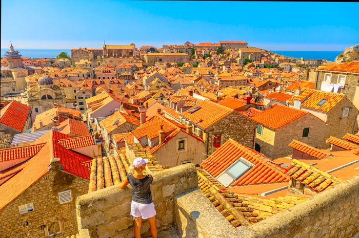 A woman gazes from behind at the picturesque red-tiled roofs of an old town.