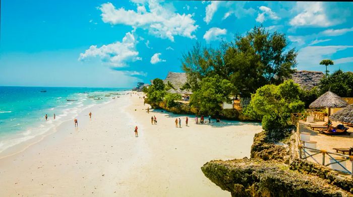 Visitors enjoying a pristine white-sand beach with straw huts in the background