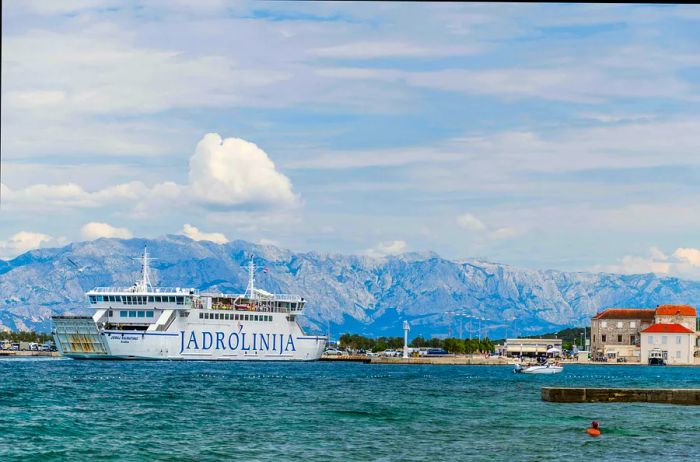 A large ferry glides past a dock on a bright summer day