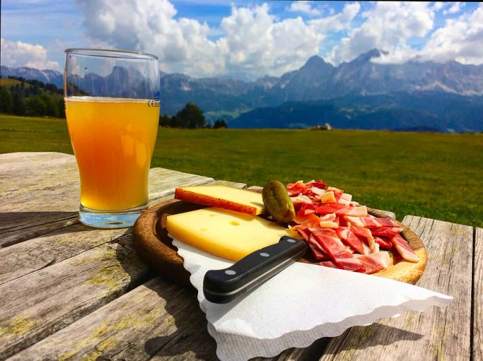 A plate adorned with cheeses paired with charcuterie, next to a refreshing beer