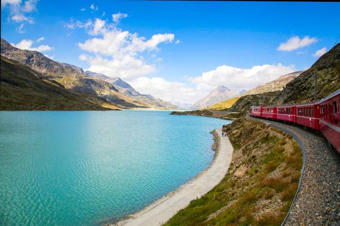 A red Bernina Express train glides along the lakeside in Switzerland.