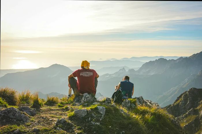 Two hikers pause to admire the scenic view in a sunny hilly area.