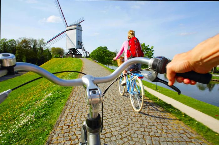 Two cyclists near a windmill, captured from the handlebars of one rider, Belgium