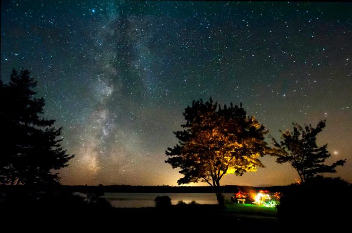 Nighttime view of friends gathered around a campfire under the Milky Way at Malay Falls, Nova Scotia, Canada © Getty