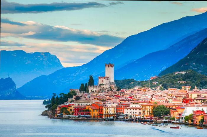 A picturesque Italian town graces the shores of Lake Garda, with majestic mountains rising in the background.