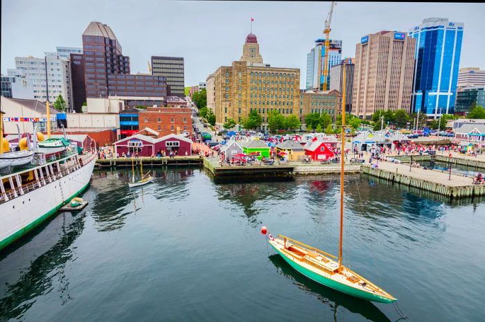 A scenic city waterfront featuring a small sailboat in the foreground