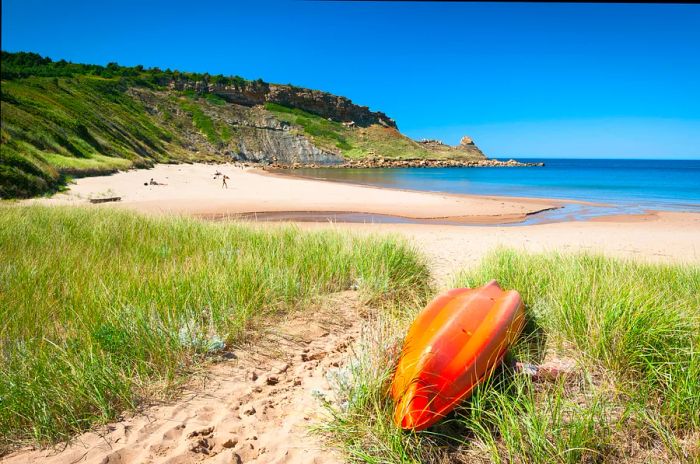 A kayak rests on the grass beside Chimney Corner Beach, Cape Breton, Nova Scotia.