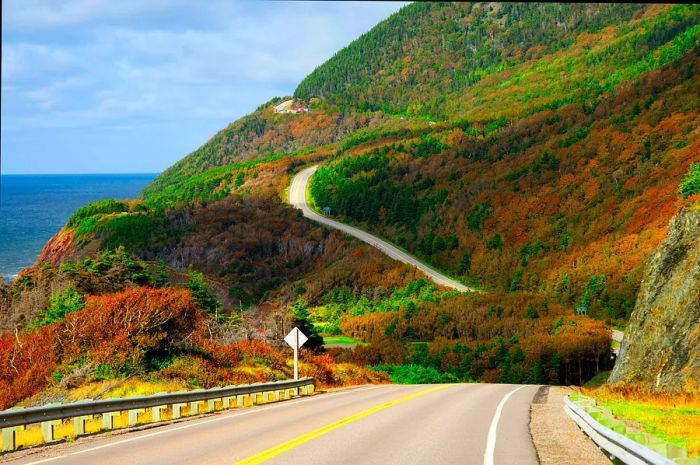 A winding road unfolds beside the sea, framed by stunning fall foliage on the other side, Cabot Trail, Cape Breton, Nova Scotia, Canada