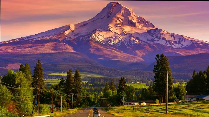 Route 35 winding towards the snow-capped Mount Hood, Oregon, at sunset, with two vehicles on the road.