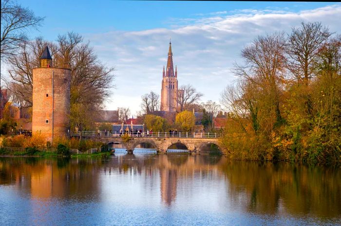 A few people stroll across a bridge in front of a church.