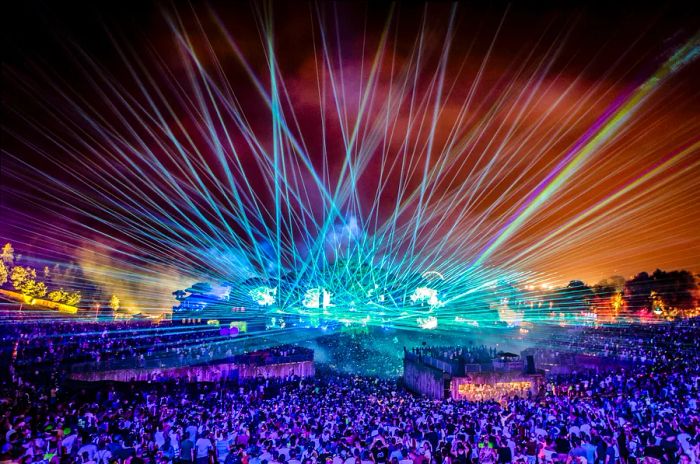 Lasers illuminate the night sky at a lively music festival, captivating a large audience.