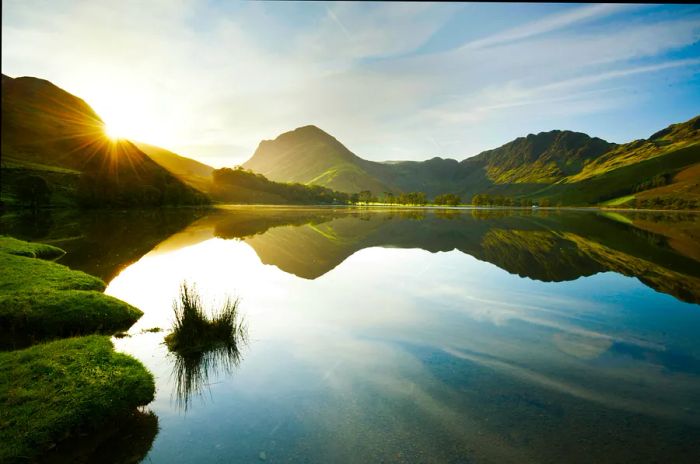 The sunlight glimmers over the gentle hills surrounding a lake in England's Lake District.