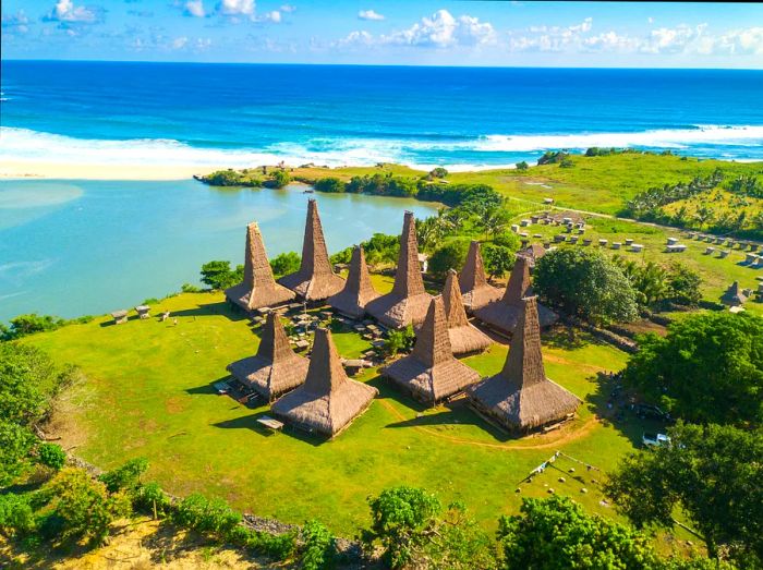 A collection of thatched huts crowned with a tall spire, perched on the edge of a tropical beach