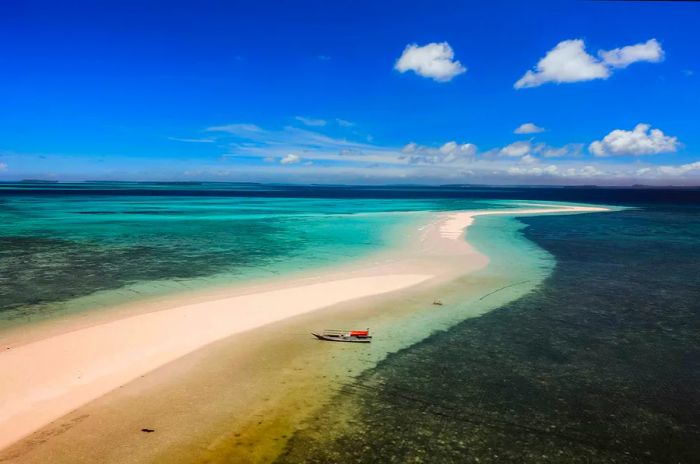 A sandbar in a turquoise sea with a small fishing boat