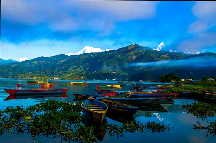 Small wooden boats drift along the shoreline of a serene lake.