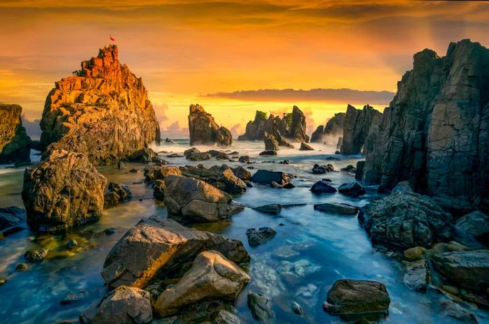 Tall, jagged rocks that resemble shark's teeth rise from the shore, with waves crashing dramatically against them.