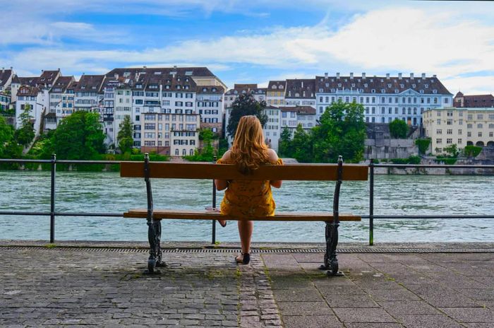 A woman relaxes on a bench beside the Rhine River in Basel, Switzerland