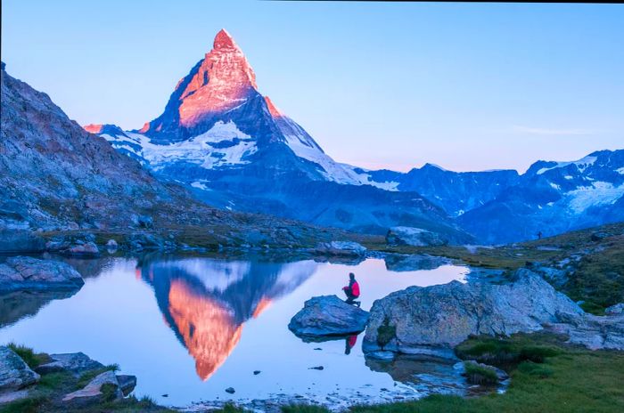 A man perched on a rock beside a lake reflecting the Matterhorn at dawn in Switzerland