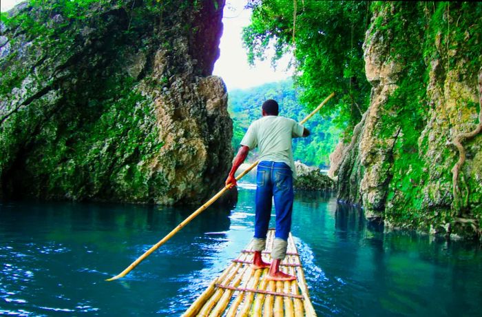 A man navigates a river on a bamboo raft