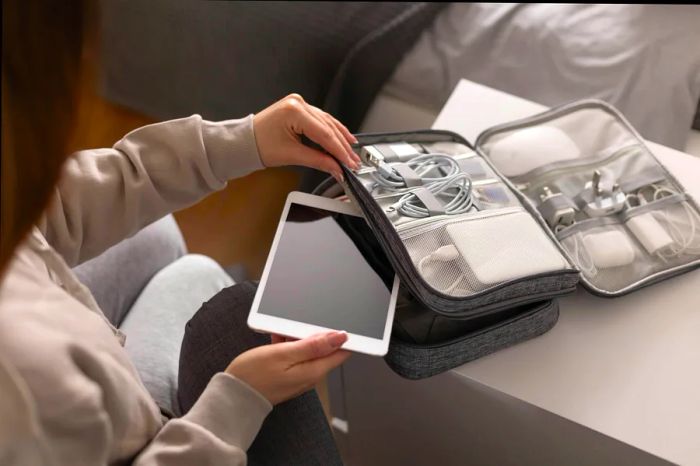 A woman is organizing a tablet alongside various cables, chargers, travel adapters, and a power bank.