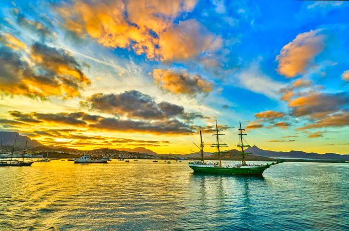 A sailboat anchored in a bay off an island at sunset