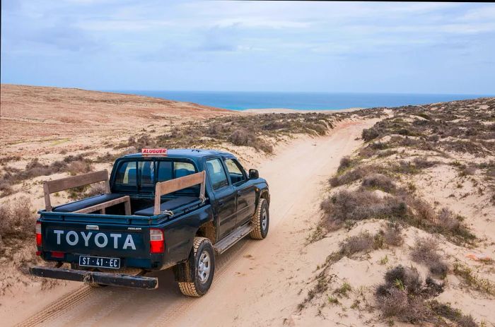 A four-wheel drive vehicle navigates a sandy path leading to the ocean