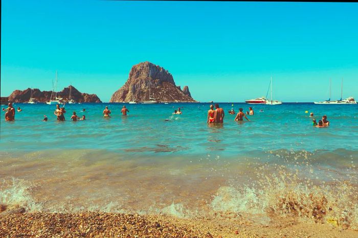 Swimmers enjoying the waters of Cala d’Hort beach, with the iconic Es Vedrà island in the background, Ibiza, Spain